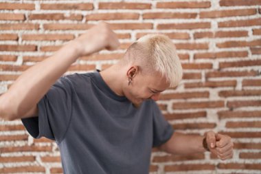 Kafkasyalı genç adam tuğlaların üzerinde duruyor mutlu ve neşeli bir şekilde dans ediyor hareketli ve kendinden emin bir şekilde müzik dinliyor. 