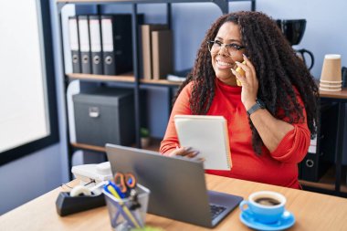 African american woman business worker talking on smartphone reading notebook at office