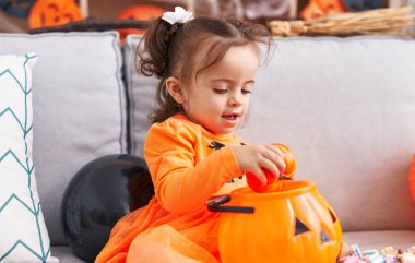 Adorable hispanic toddler having halloween party holding pumpkin toy at home