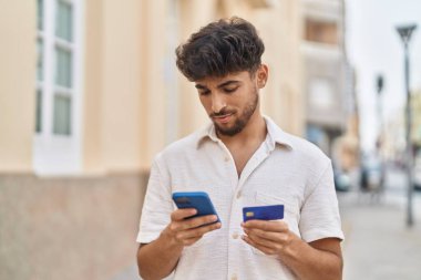 Sokakta akıllı telefon ve kredi kartı kullanan genç bir Arap.