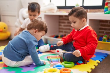 Anaokulunda yerde oturup ksilofon oynayan bir grup çocuk.