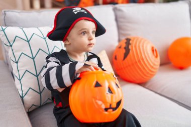 Adorable hispanic boy having halloween party holding pumpkin basket at home