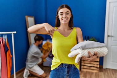 Young brunette woman holding folded laundry smiling happy pointing with hand and finger 