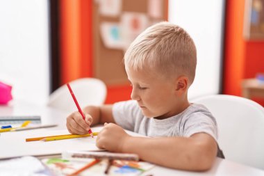 Adorable toddler student drawing on notebook sitting on table at classroom