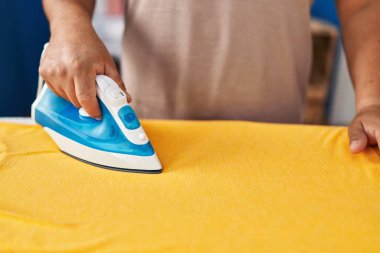 Çamaşırhanede çamaşırları ütüleyen genç Latin adam.