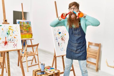 Genç kızıl saçlı adam bağırıyor ve resim stüdyosunda boyanmış avuç içini gösteriyor.