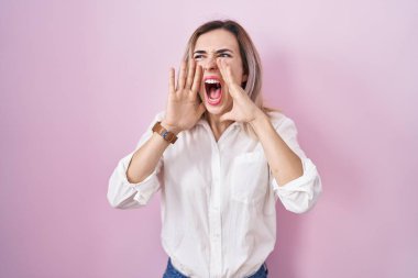 Pembe arka planda duran genç ve güzel bir kadın, elleri ağızında kızgın bir şekilde bağırıyor. 