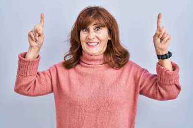 Orta yaşlı İspanyol bir kadın izole edilmiş arka planda durup şaşkın şaşkın gülüyor, parmaklarıyla işaret ediyor ve kollarını kaldırıyordu.. 