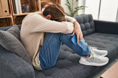 Young caucasian man patient stressed sitting on sofa at psychology clinic