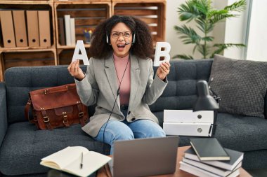 Young african american woman working speech problems at consultation office angry and mad screaming frustrated and furious, shouting with anger looking up. 
