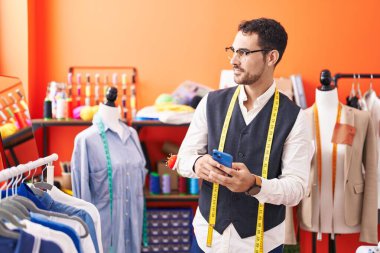 Genç İspanyol terzi atölyedeki akıllı telefonu kullanarak gülümsüyor.