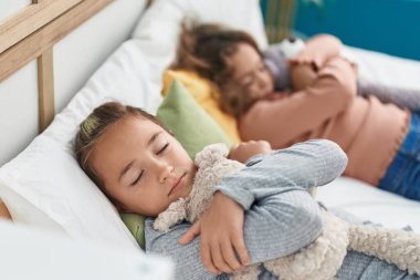 Two kids hugging teddy bear lying on bed sleeping at bedroom