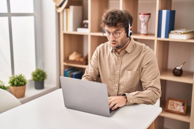Hispanic young man wearing call center agent headset scared and amazed with open mouth for surprise, disbelief face 