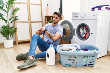 Kirli çamaşırları çamaşır makinesine koyan genç İspanyol adam kol saatini kontrol ediyor, rahat ve kendinden emin. 