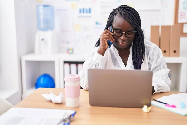 アフリカ系アメリカ人の女性ビジネスワーカーがオフィスでスマートフォンで話すノートパソコンを使って — ストック写真