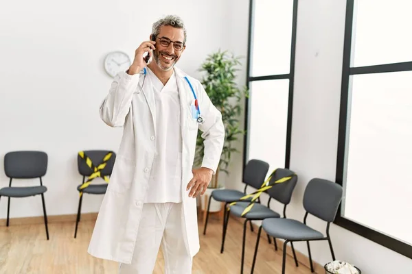 Średni Wiek Siwowłosy Mężczyzna Lekarz Uśmiecha Się Pewnie Rozmawiając Smartfonie — Zdjęcie stockowe