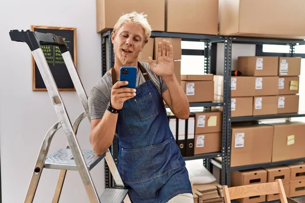 Young Blond Man Using Smartphone Working Storehouse Waiving Saying Hello — Stock fotografie