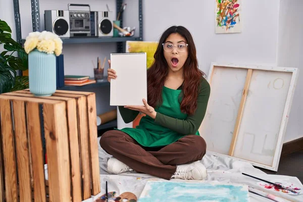 Hispanic Young Woman Holding Notebook Art Studio Scared Amazed Open —  Fotos de Stock