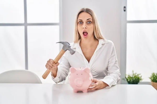 Young Blonde Woman Holding Piggy Bank Hammer Afraid Shocked Surprise — Zdjęcie stockowe
