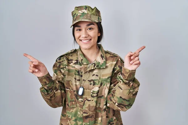 Young south asian woman wearing camouflage army uniform smiling confident pointing with fingers to different directions. copy space for advertisement