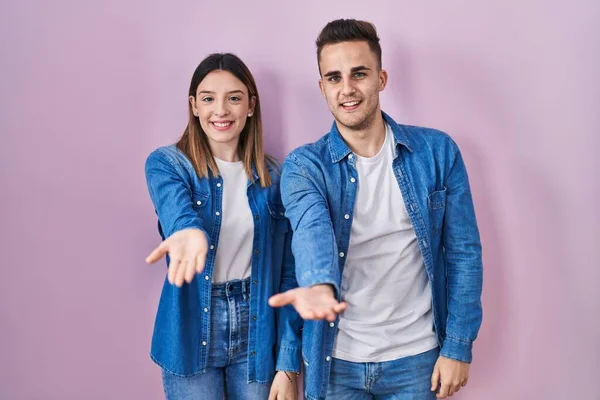 Young Hispanic Couple Standing Pink Background Smiling Cheerful Offering Palm — 图库照片