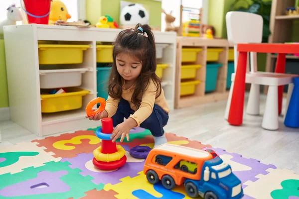 Adorable hispanic girl playing with hoops toys sitting on floor at kindergarten