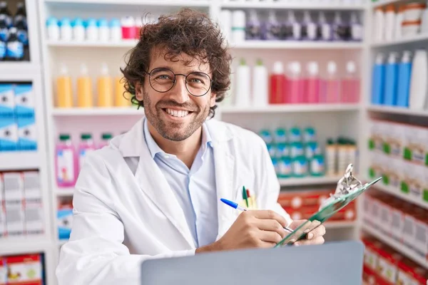 Young Hispanic Man Pharmacist Writing Document Using Laptop Pharmacy — Stockfoto