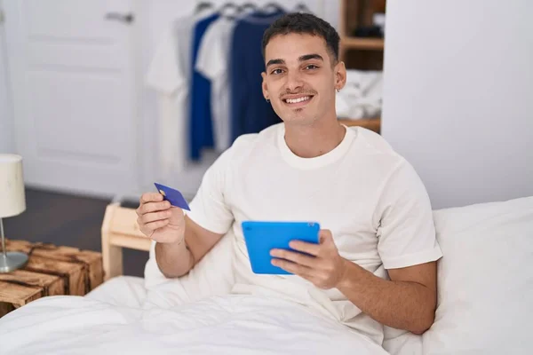 Junger Hispanischer Mann Sitzt Mit Touchpad Und Kreditkarte Auf Bett — Stockfoto