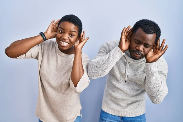 Młoda Afrykańska Para Stojąca Nad Niebieskim Tłem Próbująca Usłyszeć Obie — Zdjęcie stockowe