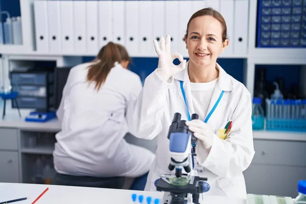 Blonde woman working on cruelty free laboratory doing ok sign with fingers, smiling friendly gesturing excellent symbol