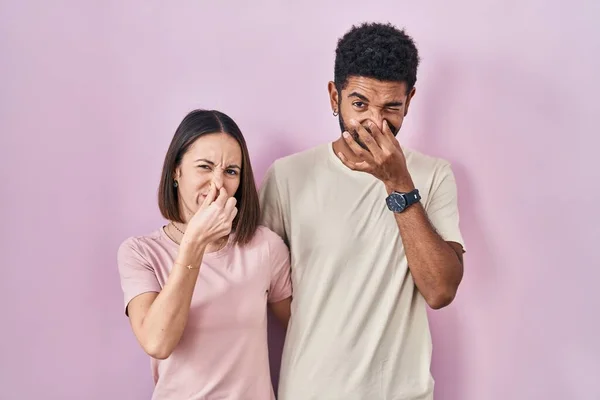 Young Hispanic Couple Together Pink Background Smelling Something Stinky Disgusting — Stockfoto