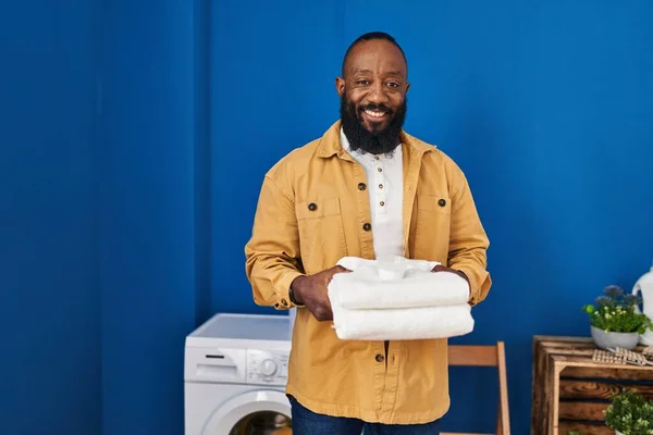 洗濯室できれいなタオルを持っているアフリカ系アメリカ人の男性は 顔に幸せとクールな笑顔で笑っています 歯を見せて — ストック写真
