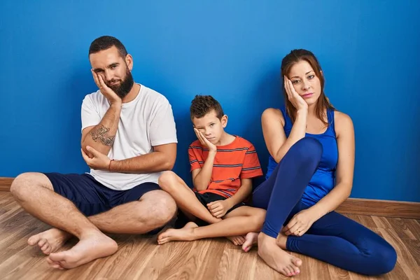 Family of three sitting on the floor at home thinking looking tired and bored with depression problems with crossed arms.
