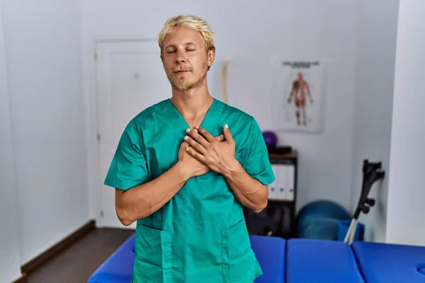 Young Blond Man Wearing Physiotherapist Uniform Standing Clinic Smiling Hands — Stockfoto