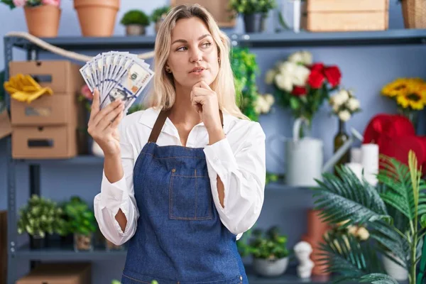 Young Blonde Woman Working Florist Shop Holding Dollars Serious Face — Stockfoto