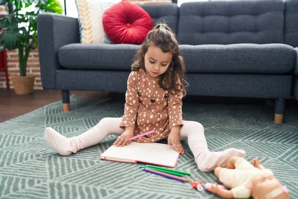 stock image Adorable hispanic girl sitting on floor drawing on notebook at home