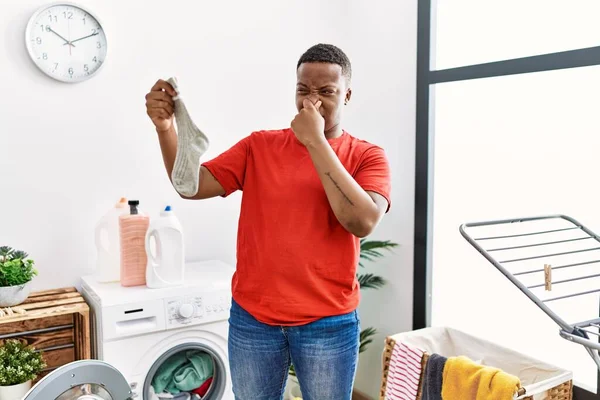 Young African Man Holding Dirty Smelly Sock Laundry Room — Stock fotografie