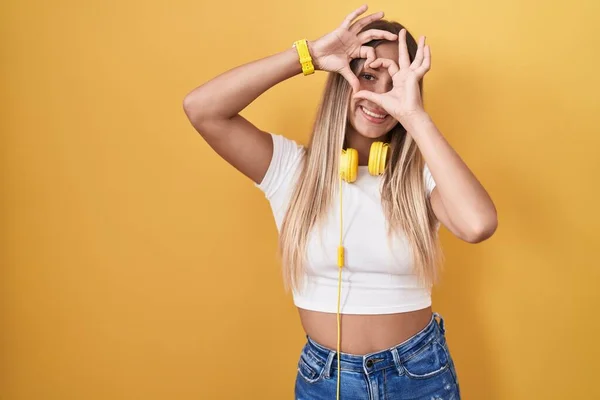 Young Blonde Woman Standing Yellow Background Wearing Headphones Doing Heart — Zdjęcie stockowe