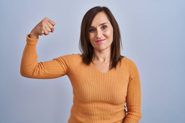 Брюнетка среднего возраста женщина, стоящая в оранжевом свитере сильный человек, показывающий мышцы рук, уверенный и гордый властью 