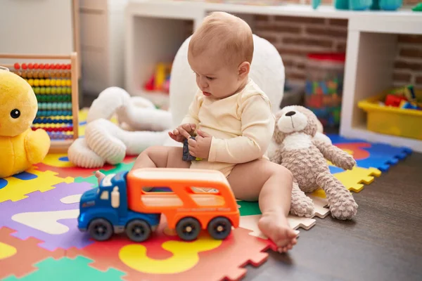 幼稚園の床に座っている車やトラックのおもちゃで遊ぶ愛らしい白人の赤ちゃん — ストック写真