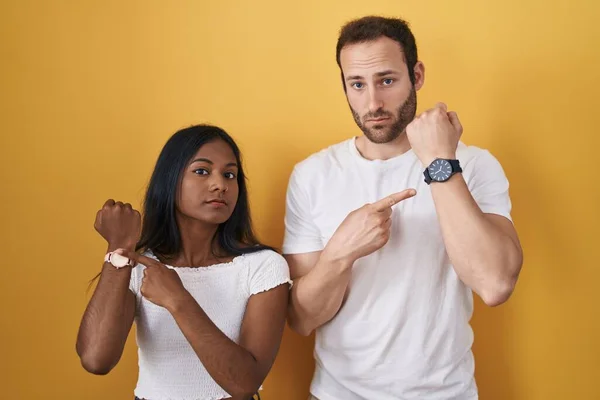 Interracial Couple Standing Yellow Background Hurry Pointing Watch Time Impatience — Stock Photo, Image