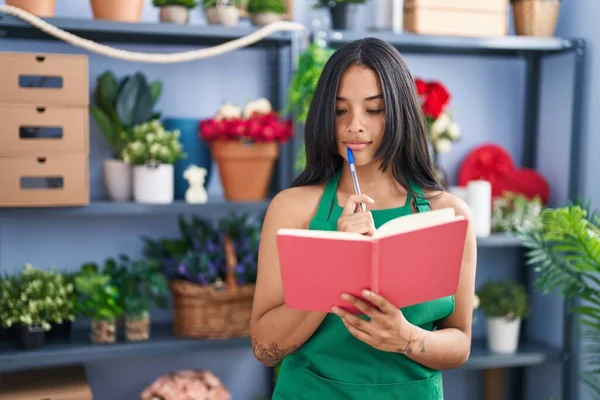 Young hispanic woman florist reading book at florist shop
