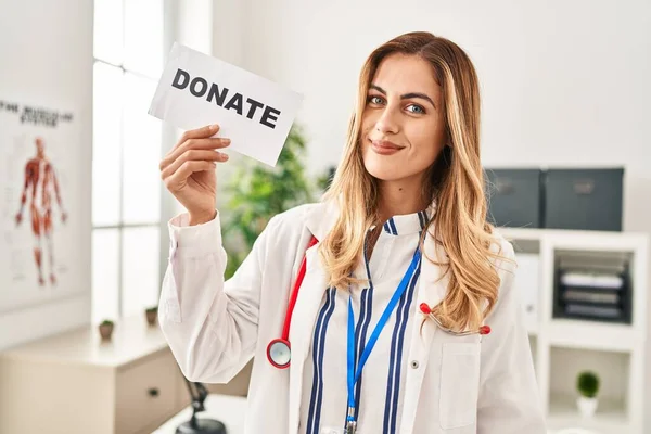 Young blonde doctor woman supporting organs donations looking positive and happy standing and smiling with a confident smile showing teeth