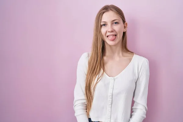 ピンク色の背景に立っている若い白人女性が面白い表情で幸せに舌を突き出しています 感情の概念 — ストック写真