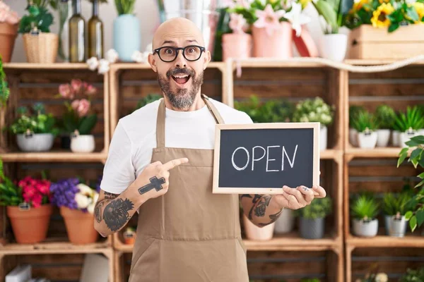 Hispanic man with tattoos working at florist holding open sign smiling happy pointing with hand and finger