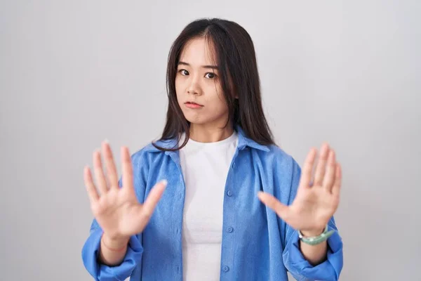 年轻的中国女人站在白种人的背景上 手心移开 脸上带着恐惧和厌恶的表情 表示拒绝和否认 停止和禁止 — 图库照片