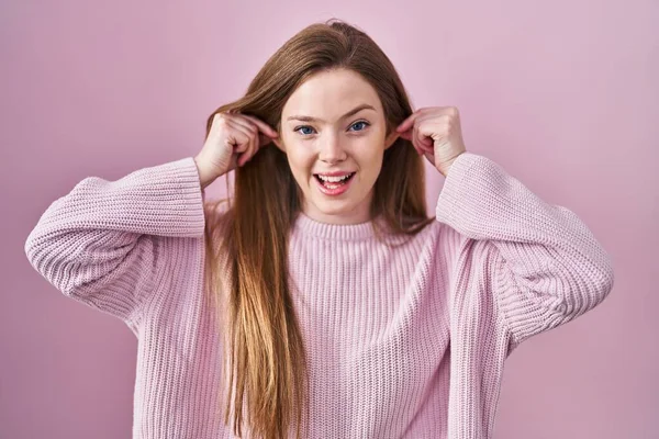 若い白人女性ピンクの背景に立って指で耳を引く笑みを浮かべて 面白いジェスチャー オーディション問題 — ストック写真
