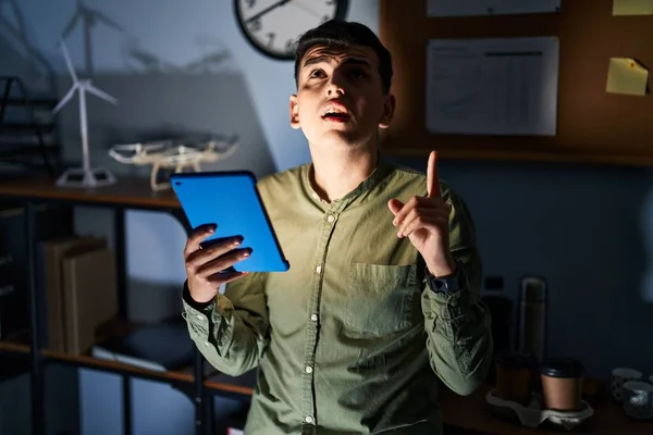 Non binary person using touchpad device at night amazed and surprised looking up and pointing with fingers and raised arms.