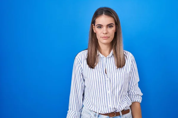 Hispanic young woman standing over blue background relaxed with serious expression on face. simple and natural looking at the camera.