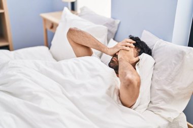 Young hispanic man suffering for insomnia lying on bed at bedroom